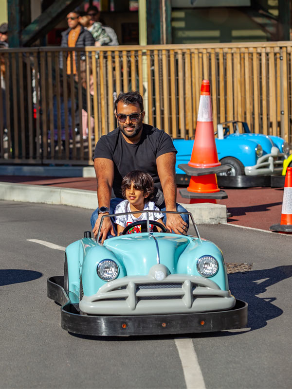 Child driving a turquoise car at Al’s Auto Academy at Paultons Park while a parent rides behind on the family driving attraction
