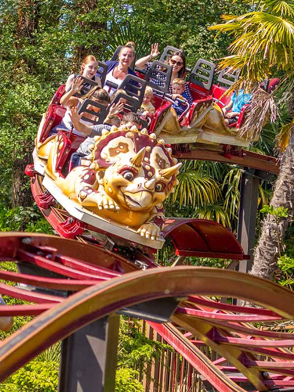 Families waving on Dino Chase roller coaster at Paultons Park as triceratops car twists through track