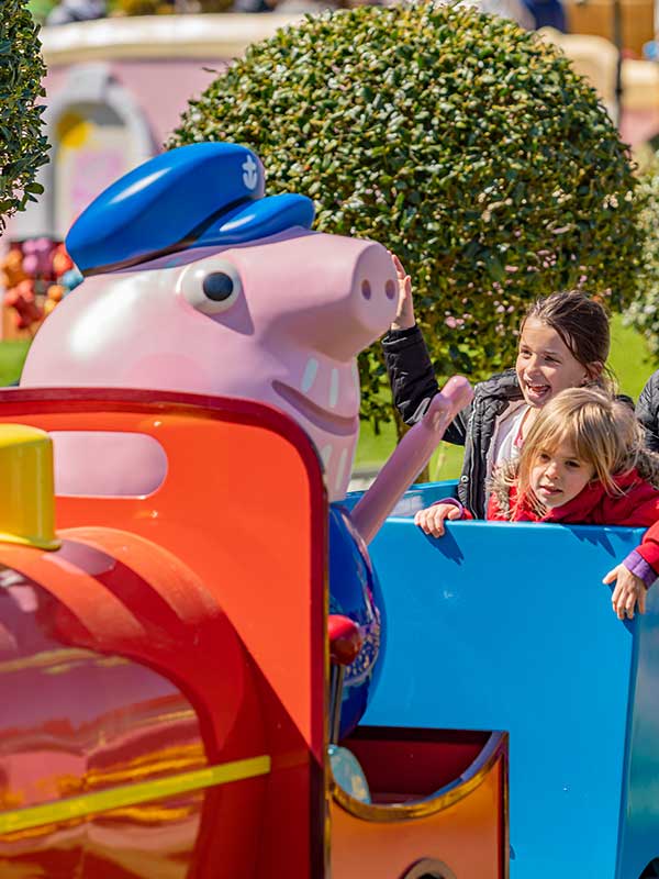 Family enjoying Grandpa Pig’s Little Train Ride in Peppa Pig World at Paultons Park with colourful train carriages and themed buildings