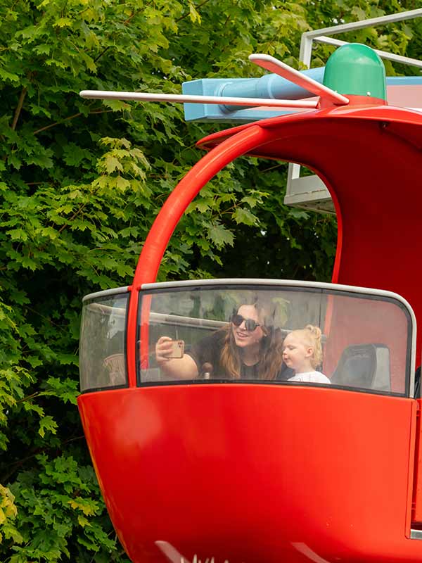 Wide shot of Miss Rabbit's Helicopter Flight at Peppa Pig World in Paultons Park with red, blue and yellow cabins rotating against a blue sky