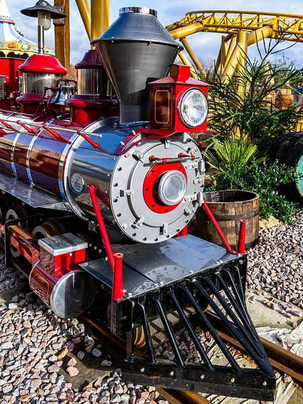 Close up of Rio Grande Train Ride engine at Paultons Park beside themed barrels and landscaping