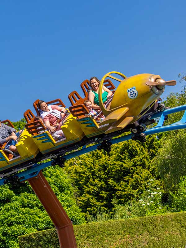Mother and child riding Farmyard Flyer roller coaster at Paultons Park on yellow plane themed train