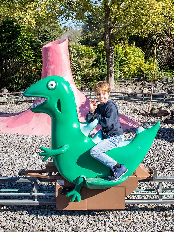 Child smiling while riding a green dinosaur on George’s Dinosaur Adventure in Peppa Pig World at Paultons Park