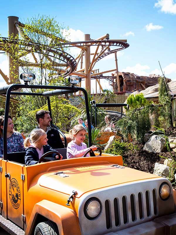 Family riding Dino Tour Co jeep past dinosaur statue in Lost Kingdom at Paultons Park