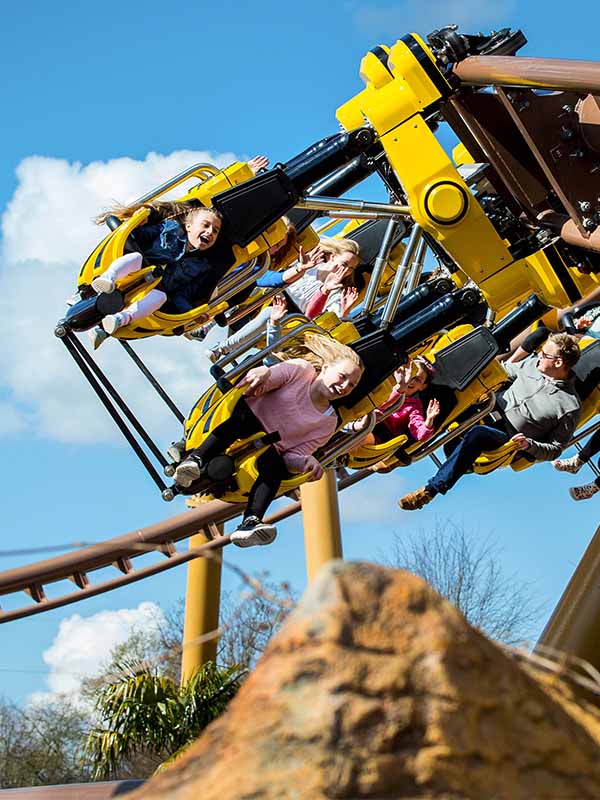Children riding Flight of the Pterosaur at Paultons Park with legs dangling as the coaster twists above rockwork