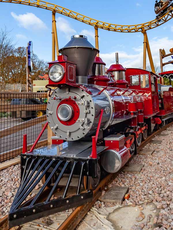Rio Grande Train Ride steam locomotive on the tracks at Paultons Park with rollercoaster track in the background