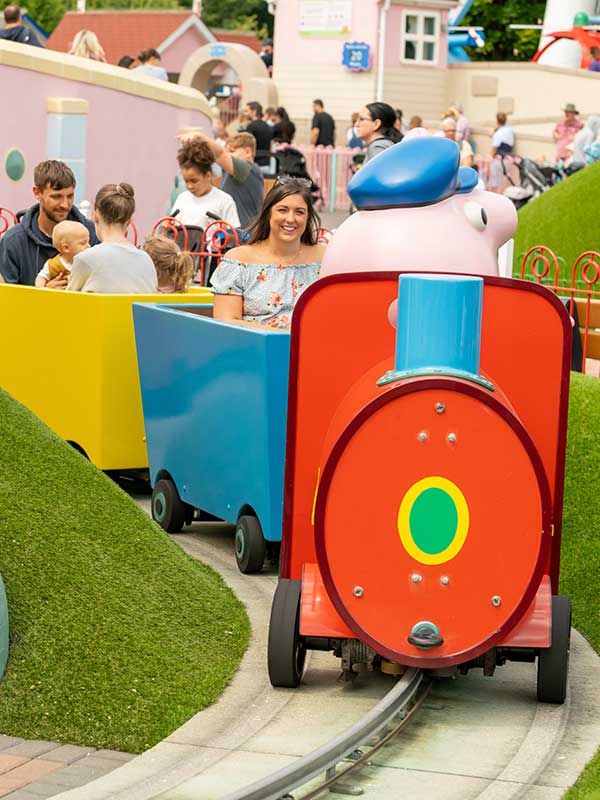 Family enjoying Grandpa Pig’s Little Train Ride in Peppa Pig World at Paultons Park with colourful train carriages and themed buildings