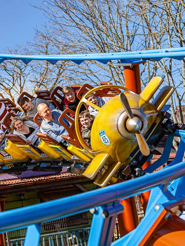Family riding Farmyard Flyer roller coaster at Paultons Park with yellow plane car banking through a curve