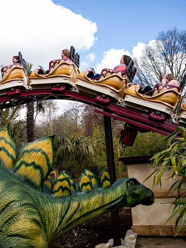 Dino Chase roller coaster at Paultons Park passing dinosaur figures in themed prehistoric area