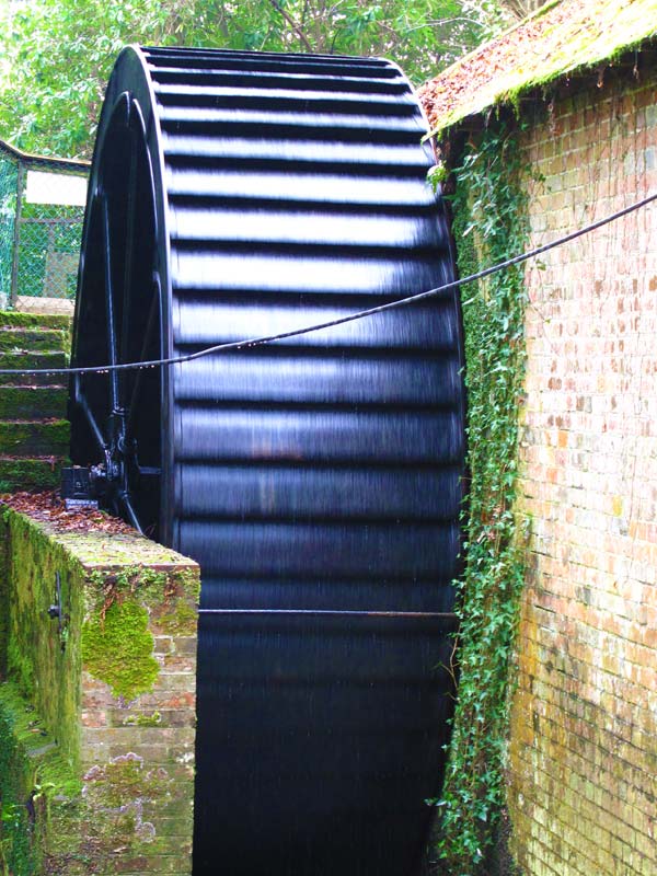 Historic water wheel surrounded by greenery at The Watermill attraction in Paultons Park
