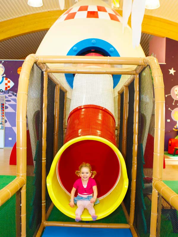 Young girl sliding down colourful tube slide in George's Spaceship Indoor Playzone at Peppa Pig World