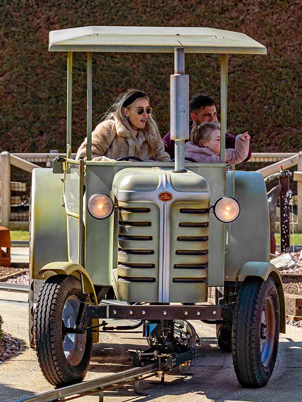 Family riding Trekking Tractors at Paultons Park with roller coaster in the background
