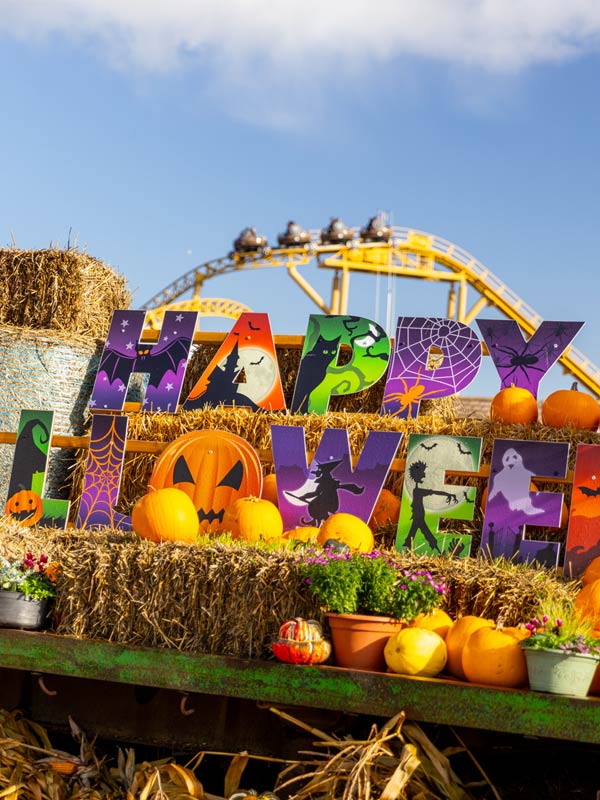 Happy Halloween display at Paultons Park with colourful themed letters, pumpkins and hay bales in front of a rollercoaster