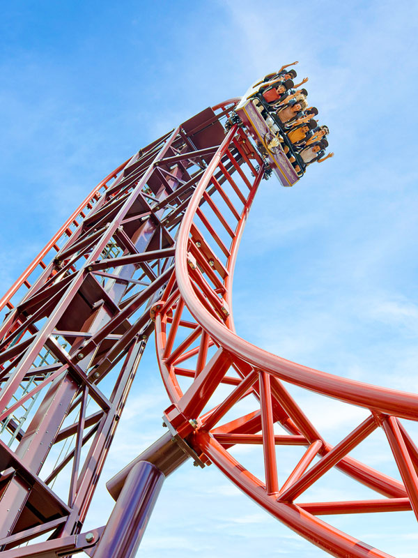 Riders on Drakon rollercoaster at Paultons Park descending the red track against a blue sky