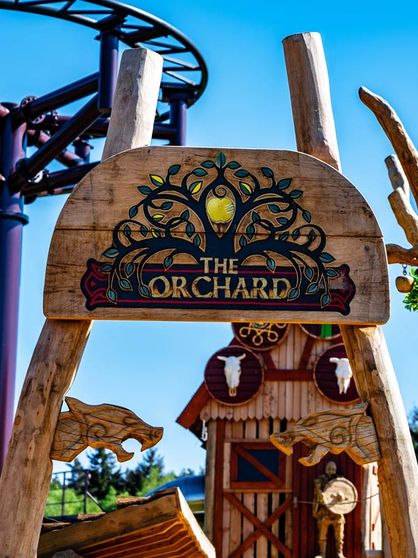 The Orchard playground sign at Paultons Park with Viking themed wooden play structures and coaster track in the background.