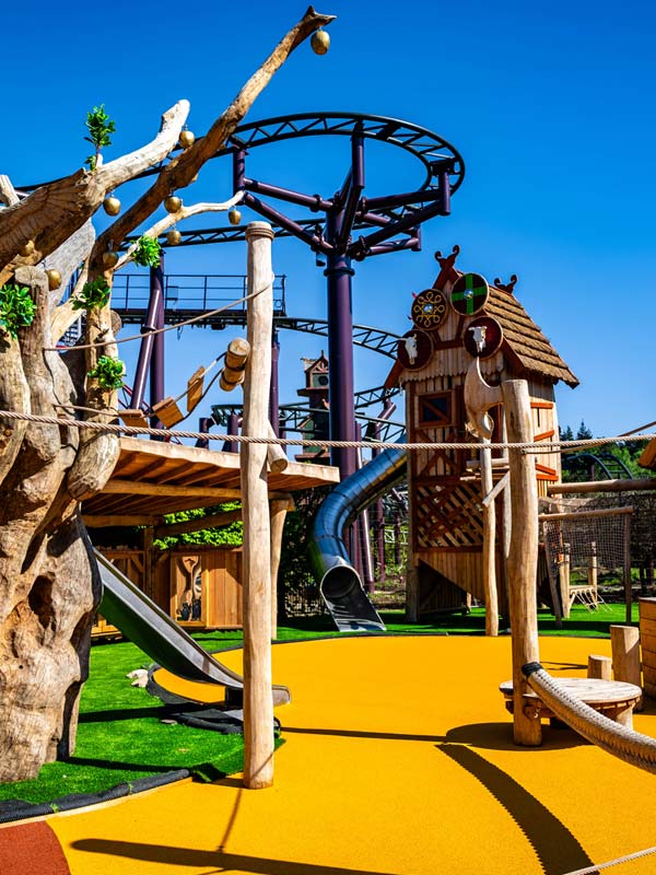 The Orchard playground at Paultons Park with Viking themed slides, climbing towers and Drakon rollercoaster track overhead.