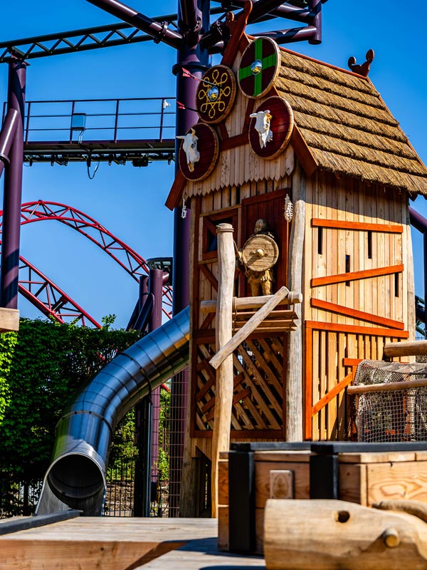The Orchard playground at Paultons Park with a Viking wooden play tower, slide and Drakon rollercoaster track behind.