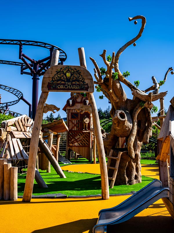The Orchard playground entrance at Paultons Park with wooden play structures, slides and a large carved tree feature.