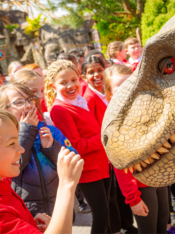 School children meeting a dinosaur character in Lost Kingdom at Paultons Park during an educational visit.
